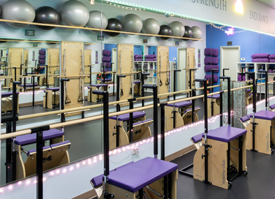 Group Pilates reformer class with instructor guiding clients through standing balance exercise
